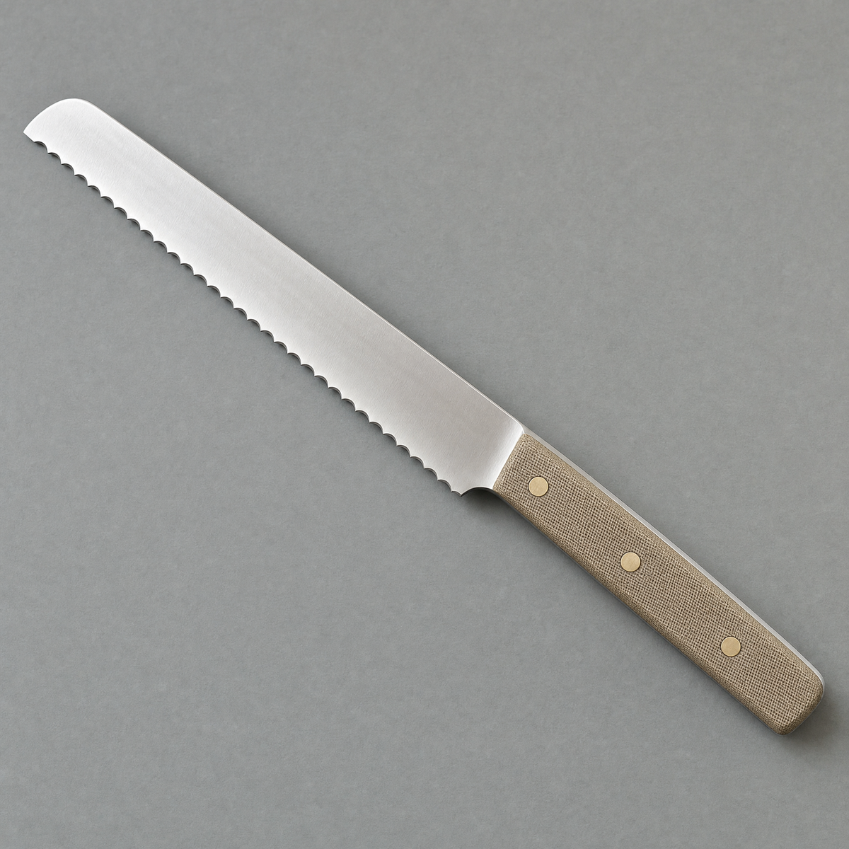 The Bread 220 seen from above: a 220 mm serrated satin stainless blade with a natural linen micarta handle on three brass pins.