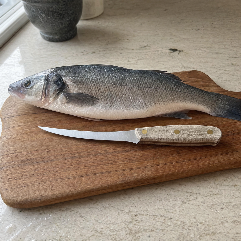 The Boning 150 on a wooden board beside a whole sea bass.