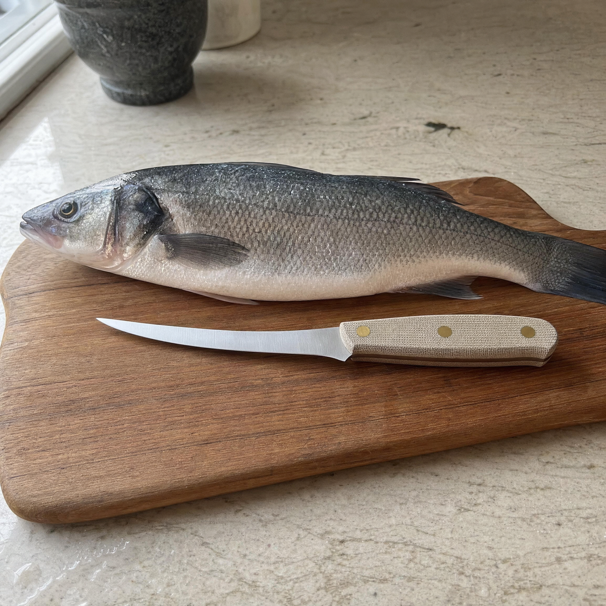 The Boning 150 on a wooden board beside a whole sea bass.