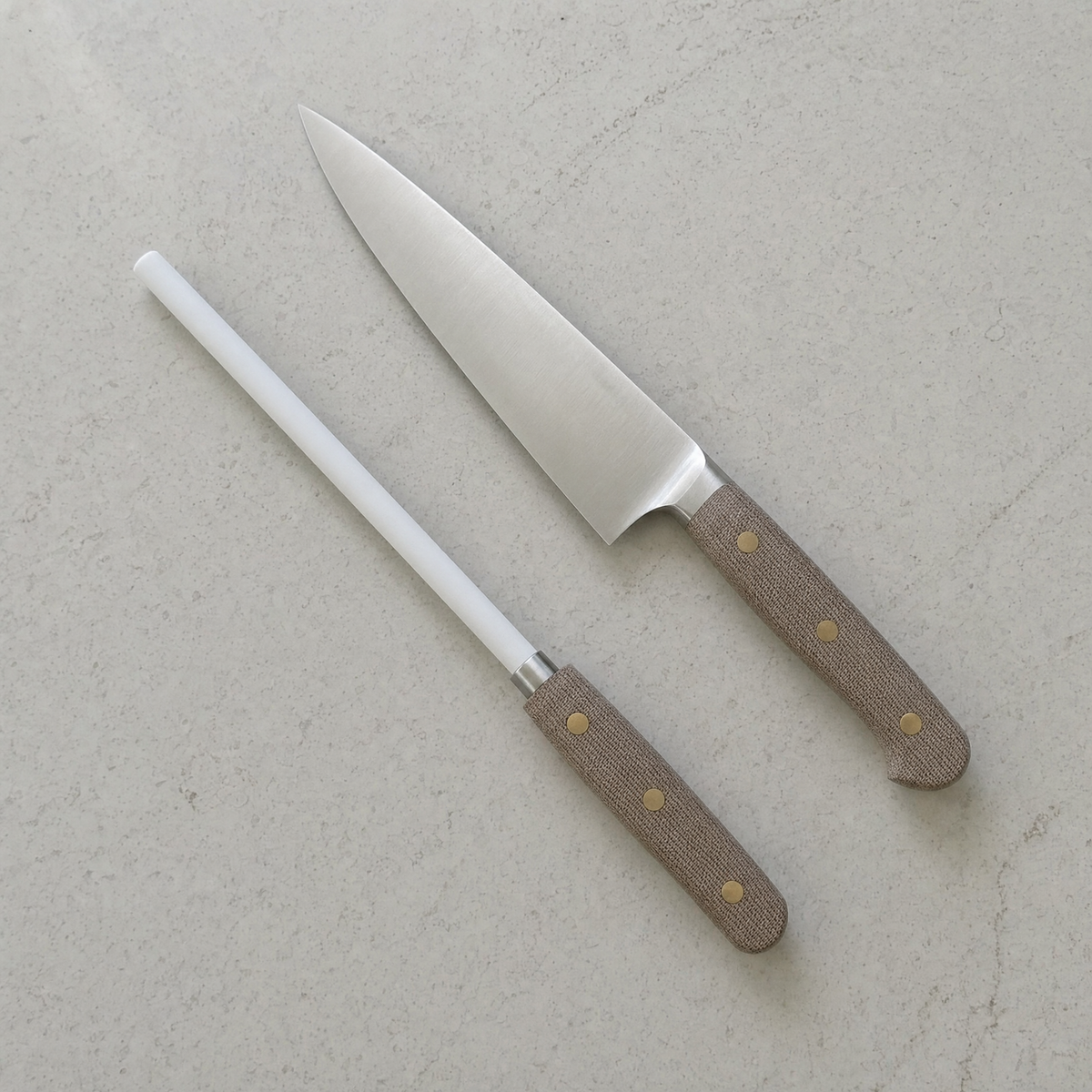 The honing rod lying on a worktop beside a chef's knife with a matching linen micarta handle.