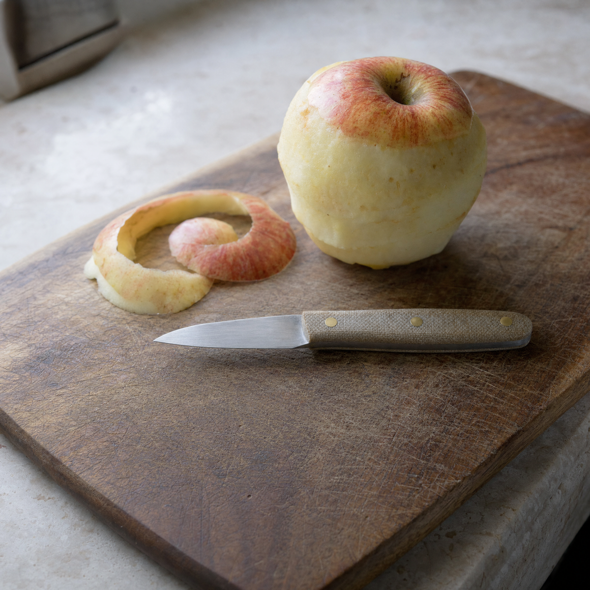 The Paring 90 on a board beside a part-peeled apple and a curl of peel.