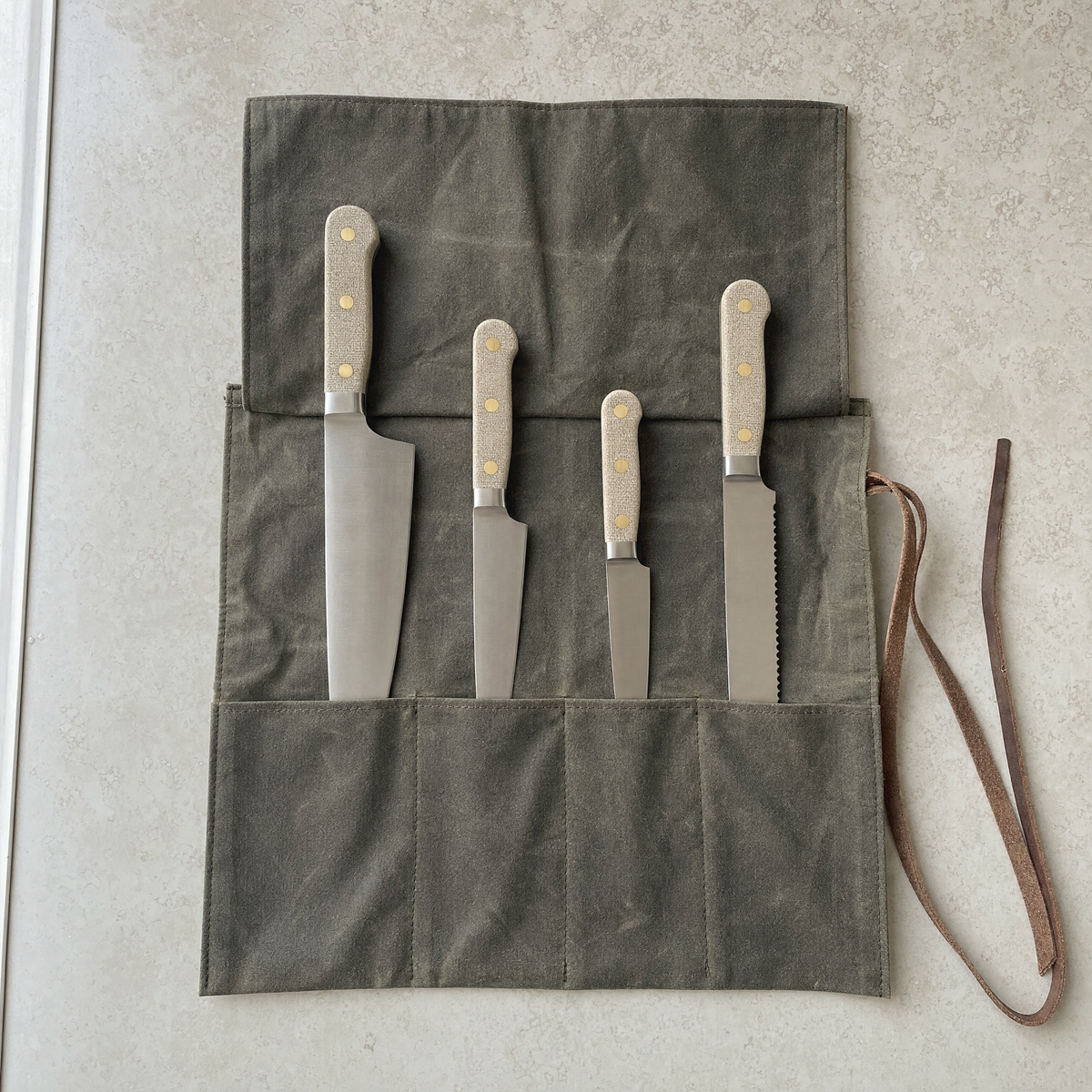 All four knives of the set seated one per slot in the open waxed canvas roll, chef to bread knife.
